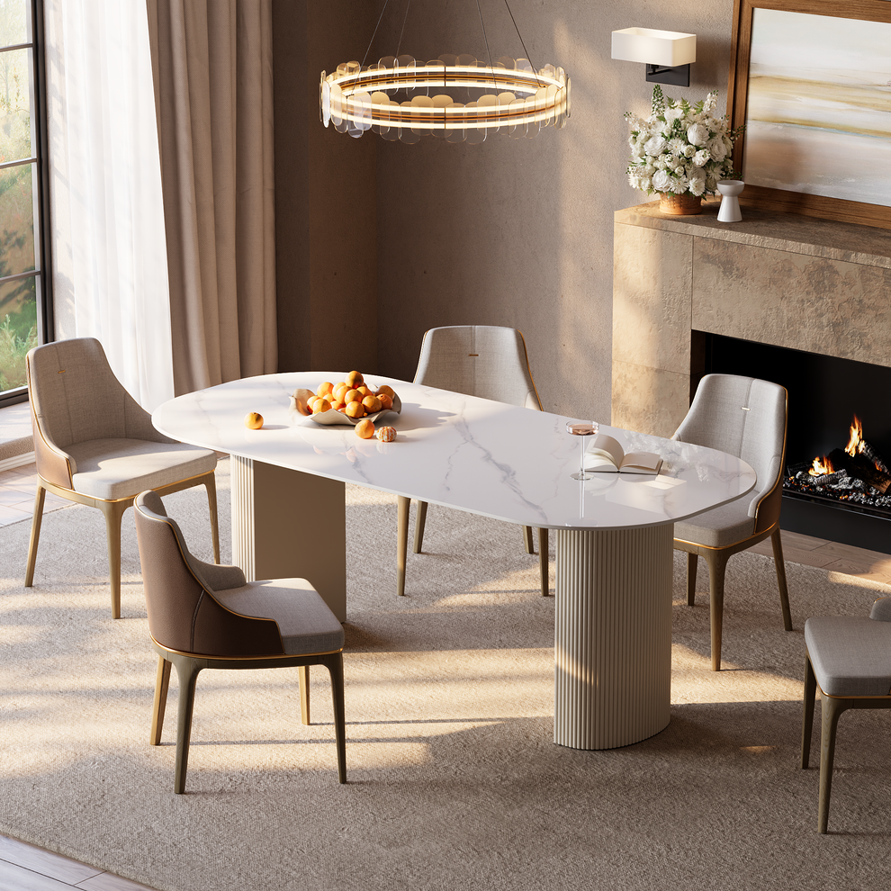 White veined dining table with a rounded rectangular top and fluted pedestal supports beside a fireplace