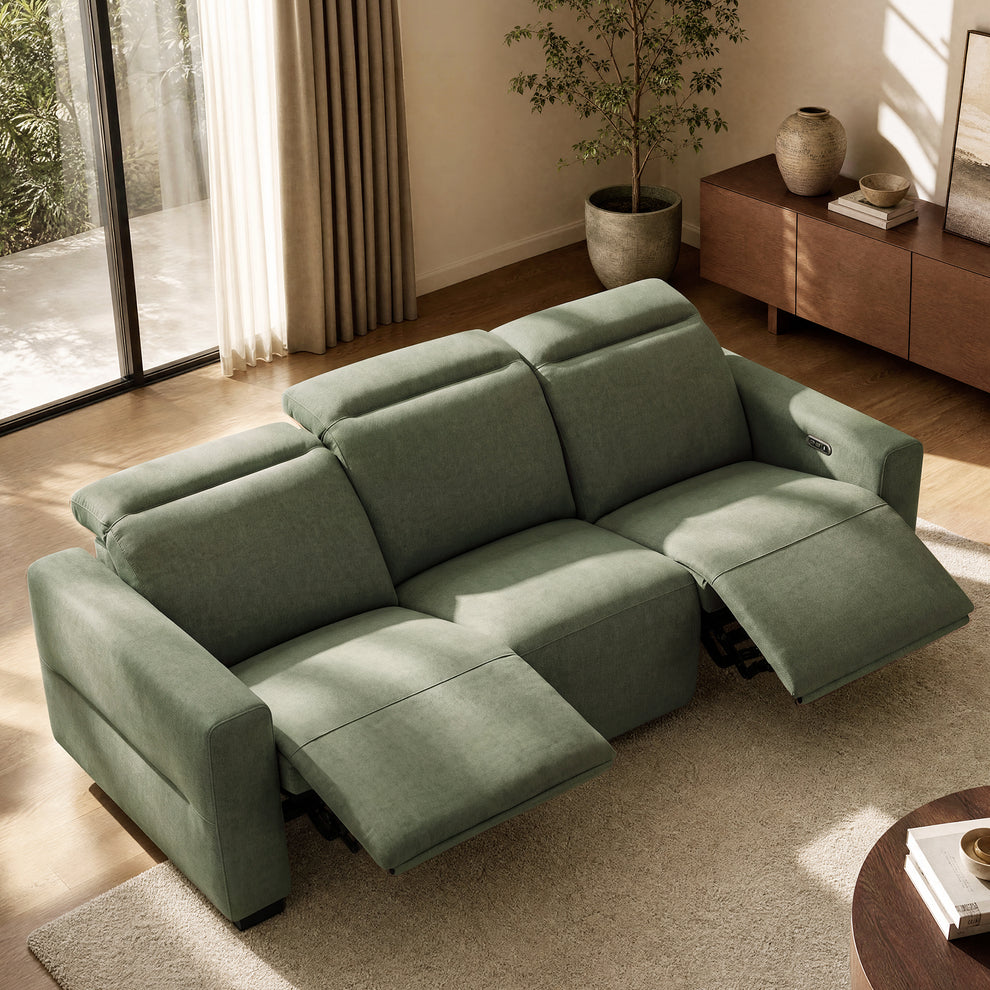 Green three-seat reclining sofa with two footrests extended in a sunlit living room.