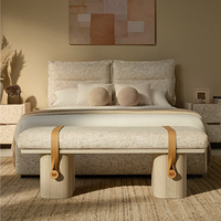 Beige upholstered bench with tan accent straps and pale rounded supports at the foot of a matching bed