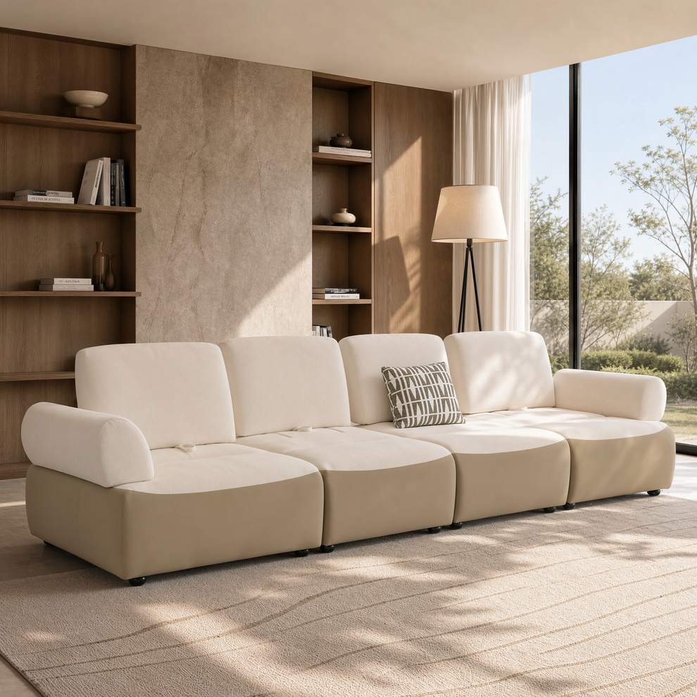 Cream four-seat sofa with rounded arms and a patterned cushion in a sunlit room with built-in shelves, a floor lamp and tall windows.