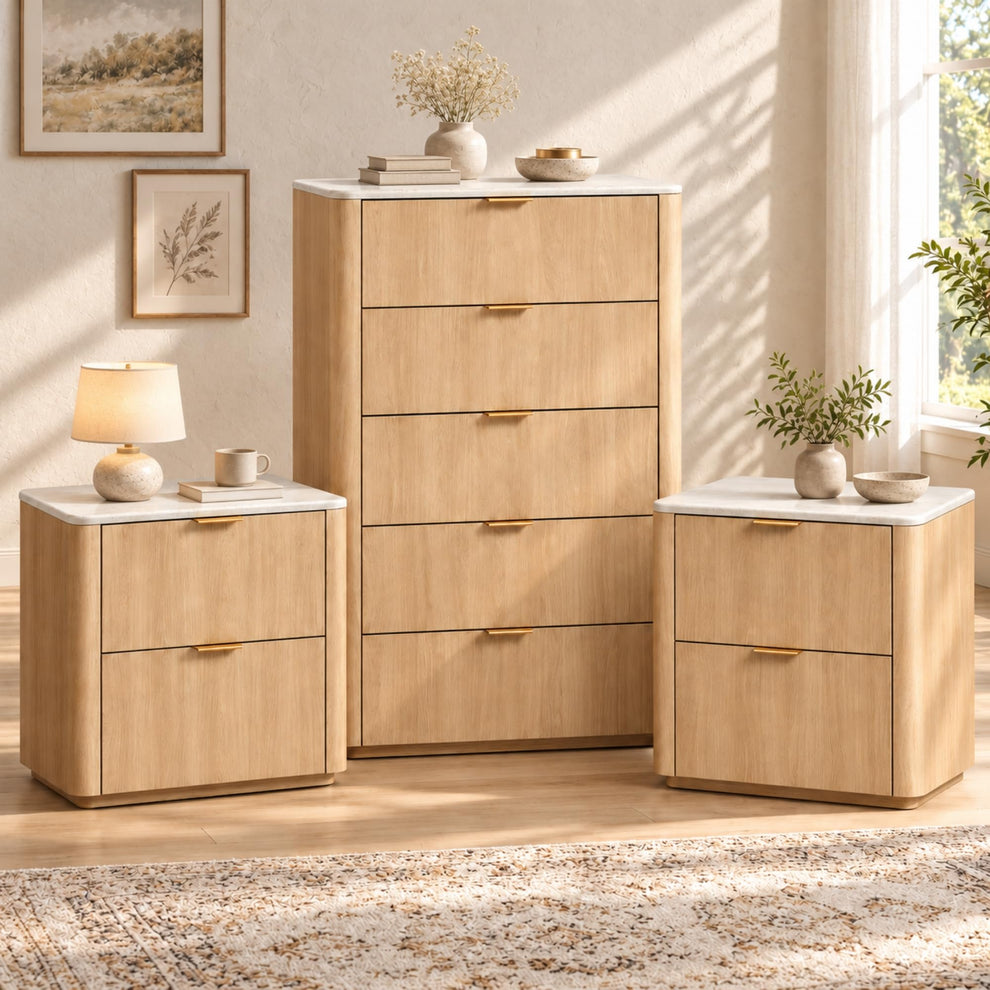 A tall five-drawer chest stands between two matching two-drawer cabinets, all with light wood-grain fronts, white tops and gold-colored handles, in a sunlit room.