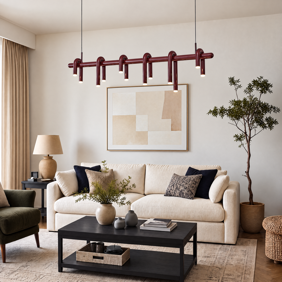 Burgundy pendant light with curved tubular arms and glowing downward tips hangs above a cream sofa in a living room with a black coffee table, framed abstract art and a potted tree.