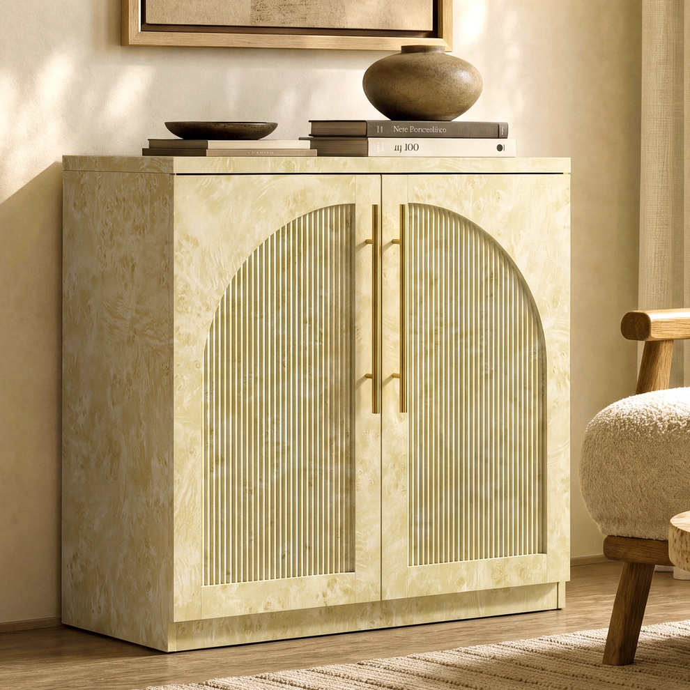 Pale mottled accent cabinet with arched fluted double doors and gold-tone handles beside an upholstered chair