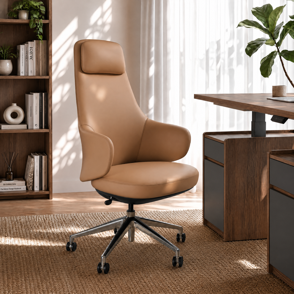 Tan high-back office chair with a padded headrest, curved armrests and a five-spoke wheeled base beside a desk in a sunlit room with bookshelves and plants.
