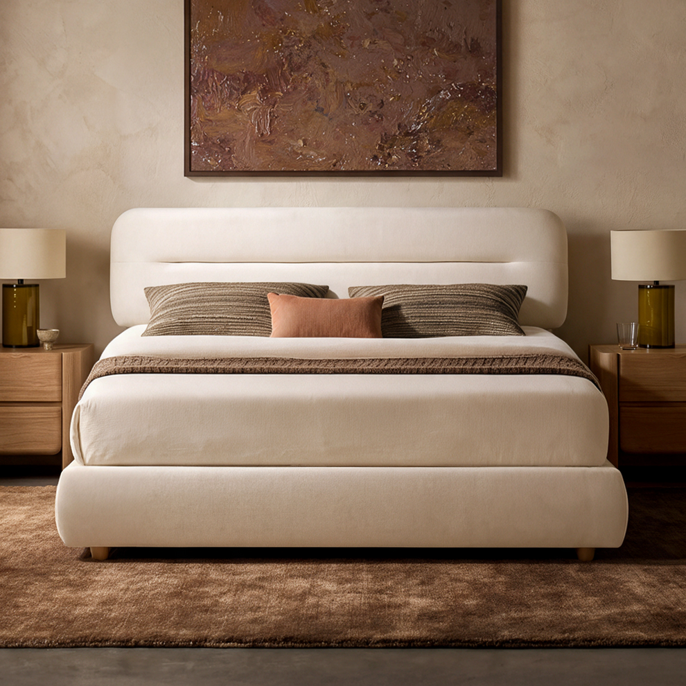 A cream upholstered bed with a rounded headboard is centered between wooden nightstands, with striped and rust-colored pillows, matching lamps, and a framed painting above.