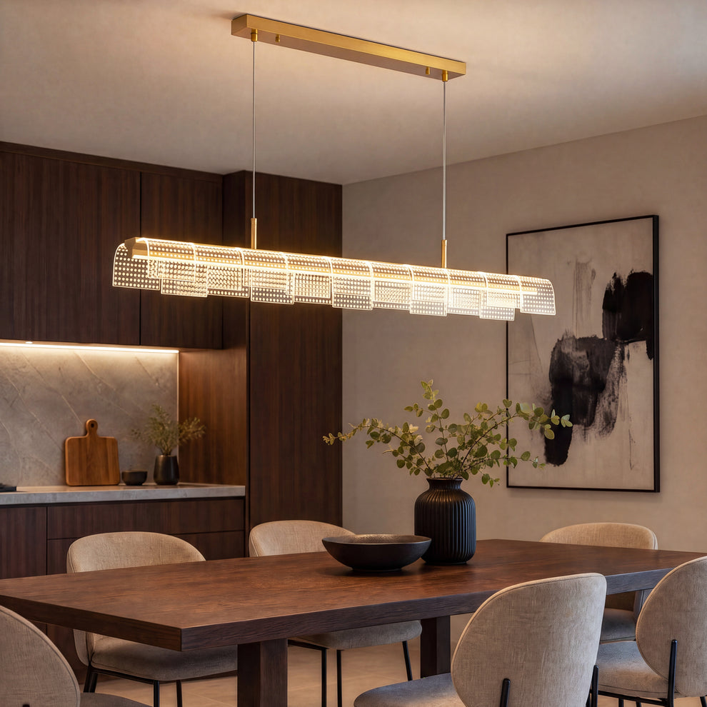 An illuminated linear pendant with gold-colored fittings and overlapping dotted panels hangs above a dark dining table surrounded by beige chairs.