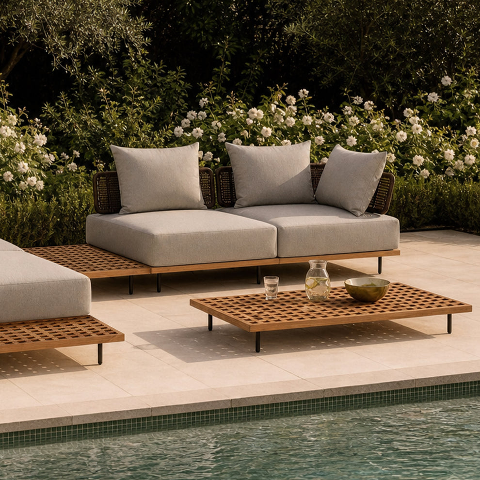 Two-seat outdoor sofa with three pillows stands behind a low lattice-top table beside a pool
