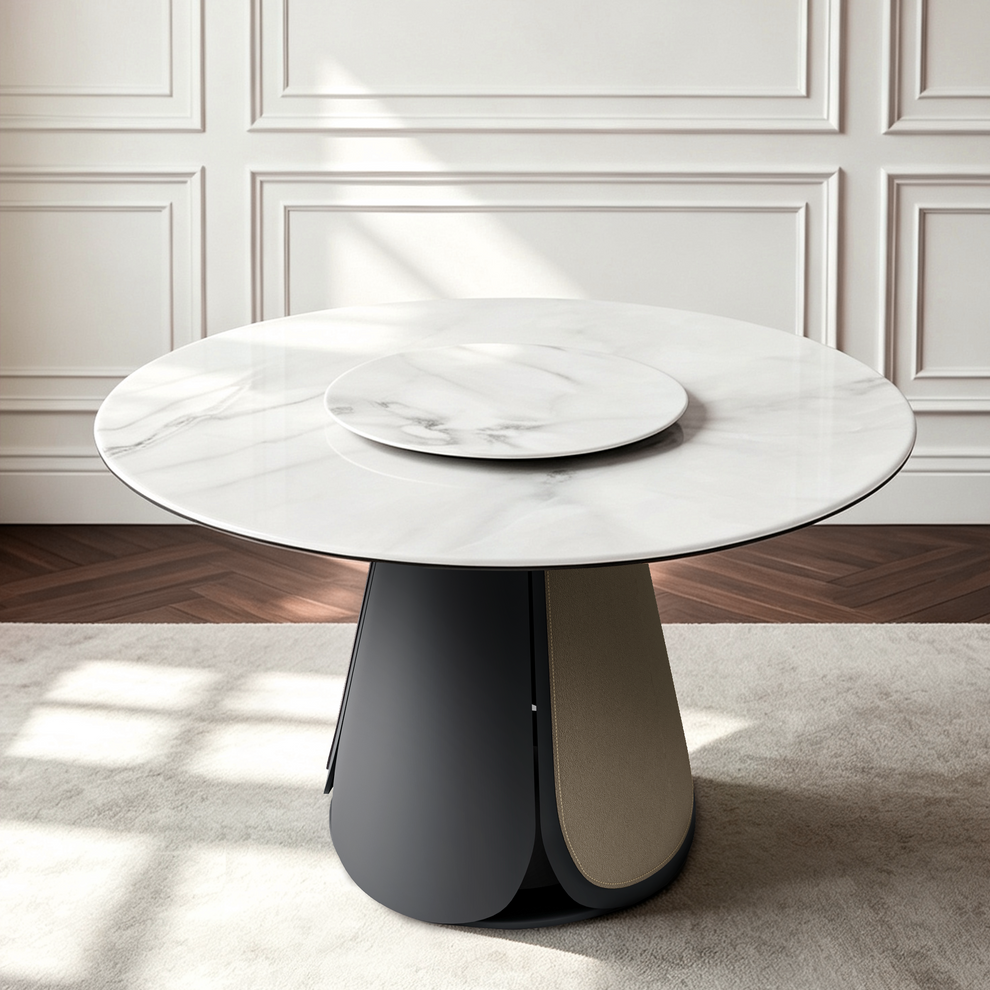 Round white marble-pattern table with a dark sculptural pedestal base in a bright room