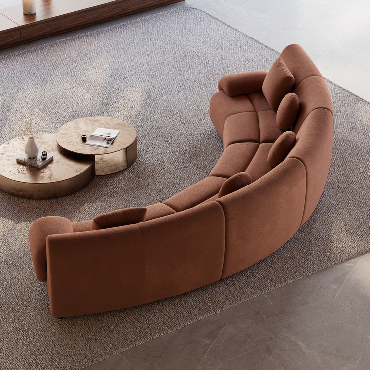 Overhead view of a curved rust-colored sofa with matching cushions on a textured gray rug beside two overlapping round coffee tables.