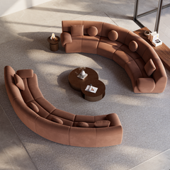 Overhead view of two curved brown sofas with round and square cushions facing two overlapping round coffee tables on a large light-colored rug.