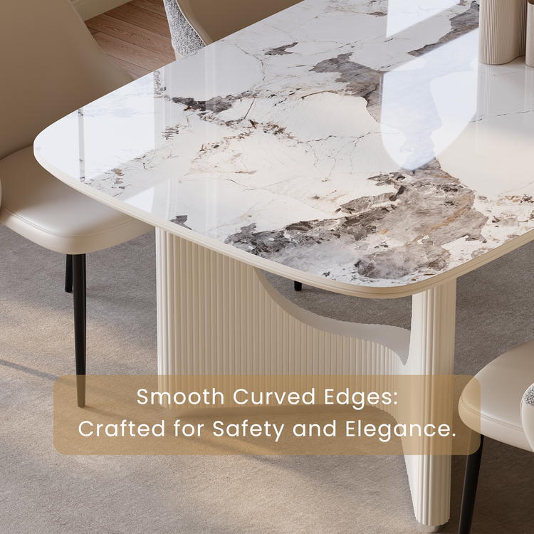 Close-up of a table with rounded corners, a glossy white top patterned with gray and beige veining, and a cream ribbed base, surrounded by beige chairs.