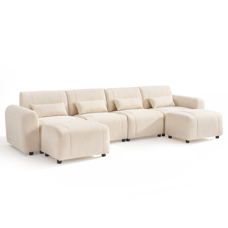 Cream-colored sofa with four back cushions, four rectangular pillows, rounded arms, short black feet, and two matching ottomans positioned in front of the outer seats.