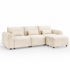 Cream-colored sofa with three back cushions, three rectangular pillows, rounded arms, short dark legs, and a matching ottoman positioned in front of the right seat.