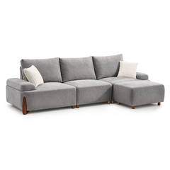 A gray sectional sofa with three back cushions, two white throw pillows, and a matching ottoman on a white background.