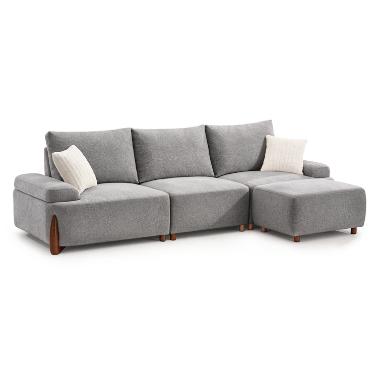 A gray sectional sofa with three back cushions, two white throw pillows, and a matching ottoman on a white background.