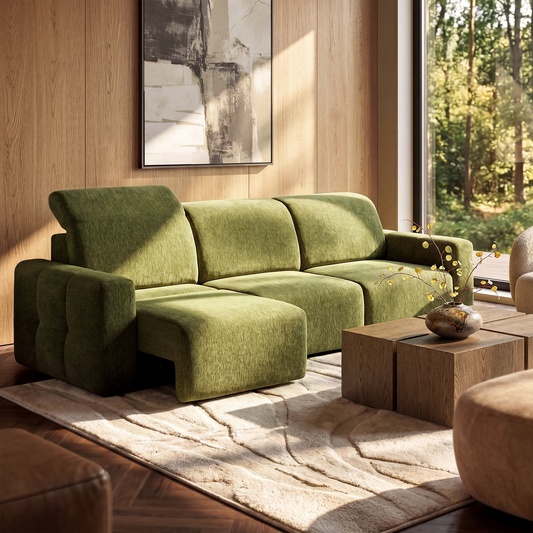 Olive-green sectional sofa with a chaise lounge in a sunlit living room, beside wood tables and a vase of branches.