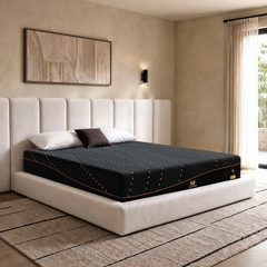 Black patterned mattress with gold-tone piping on a cream upholstered bed beside a bright bedroom window