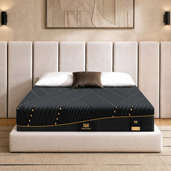 A patterned mattress rests on a platform bed beneath three pillows and a tall paneled headboard