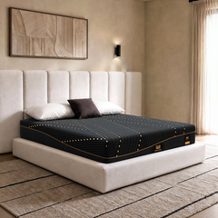 Black mattress with gold piping rests on a cream upholstered bed beneath two white pillows