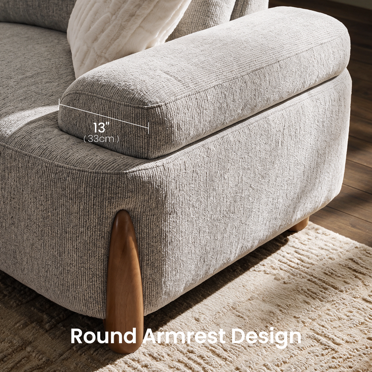 Close-up of a light gray sofa with a broad, rounded armrest marked as 13 inches (33 cm) wide, textured upholstery, a white cushion and a tapered brown leg.