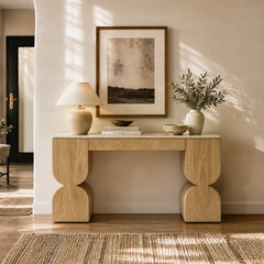 Sculptural light wood console table styled with a lamp, books, vase, and framed art.