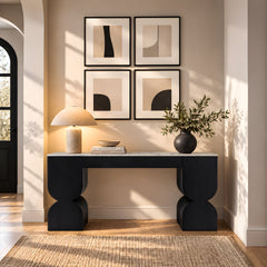 Black sculptural console table styled with a lamp, books, and leafy vase.