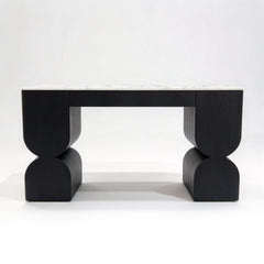 Black sculptural wood table with curved supports and a white marble-patterned top.