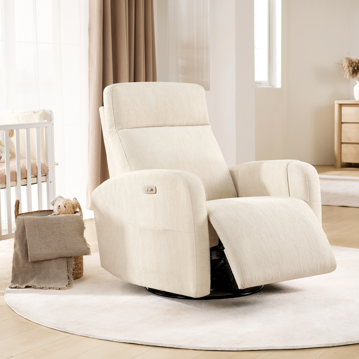 Beige reclining chair with an extended footrest, rounded arms and side controls beside a crib in a bright nursery