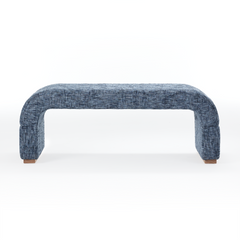 A blue plaid upholstered bench has rounded waterfall sides, Small brown feet appear beneath both ends