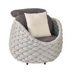 Round lounge chair has a wide woven surround, dark cushions, and a light throw pillow