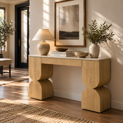Light wood console table with sculpted legs in a sunlit entryway.