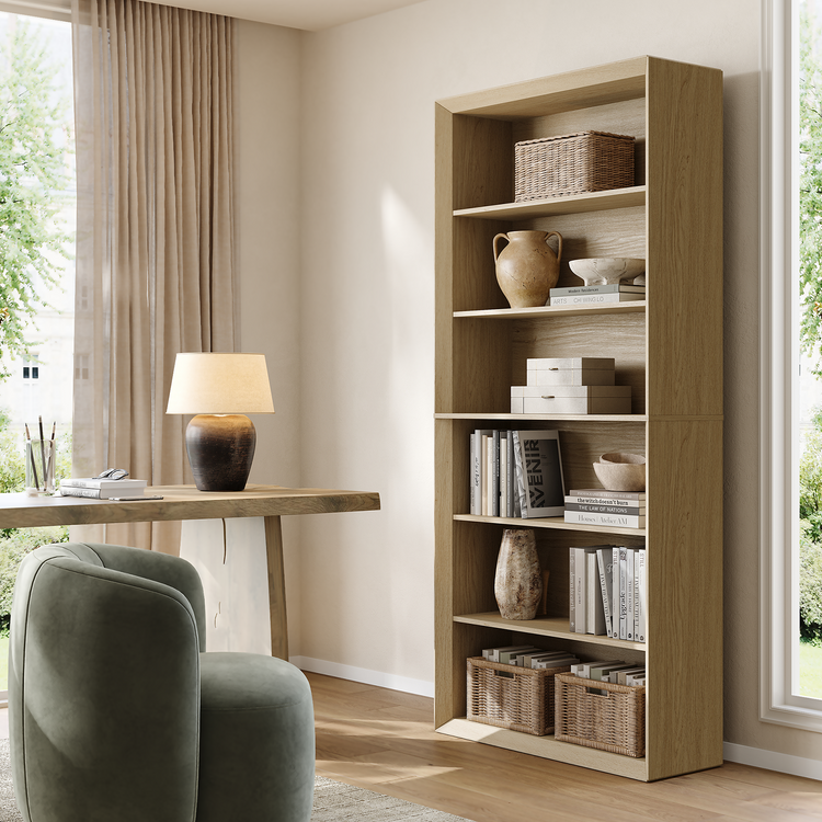 Tall pale wood open bookcase filled with books and decor beside a green chair