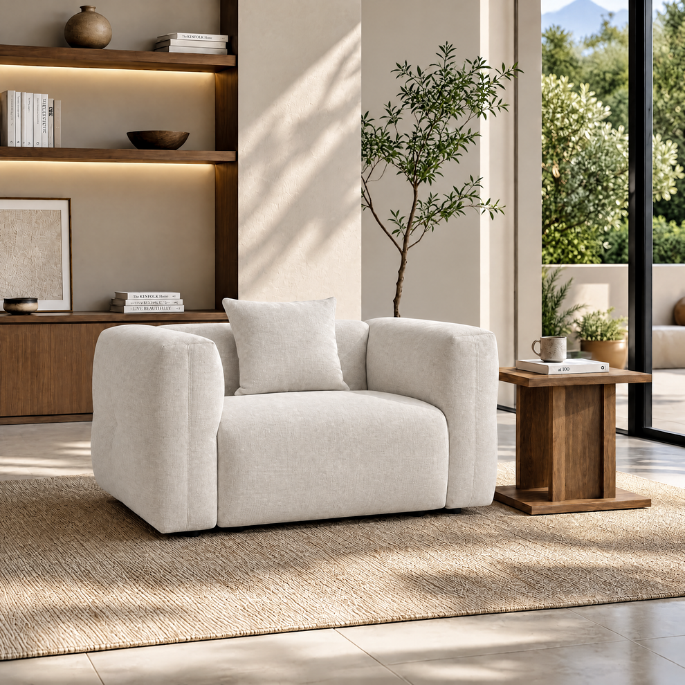 White upholstered armchair with broad arms and a matching cushion in a sunlit living room.