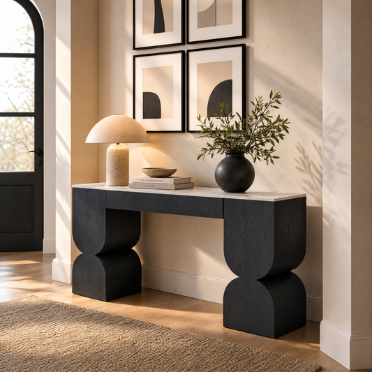 Black sculptural console table styled with a lamp, books, bowl, and leafy vase.