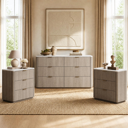 A six-drawer dresser and two matching three-drawer chests with pale tops and gold-colored handles stand beneath abstract wall art, styled with a lamp, vases, books and a bust.