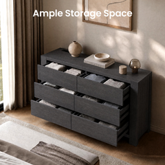A dark, wide dresser with six open drawers holding folded clothing stands against a wall; a vase, bowl, books, and small decorative objects sit on top.