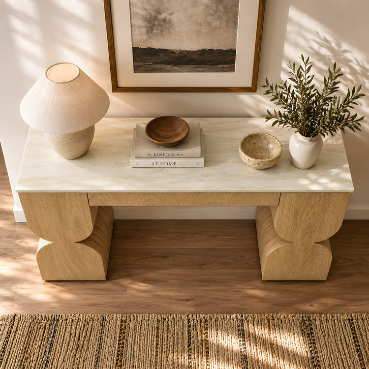 Wood console table styled with a lamp, bowls, books, and leafy branches.