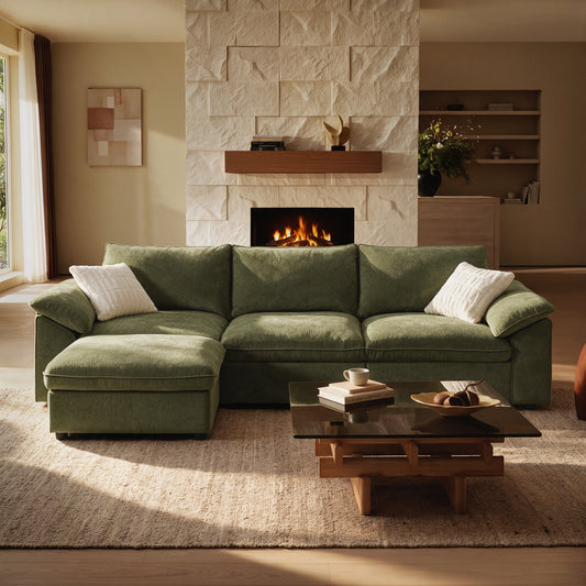 Olive-green sectional sofa with a chaise and two white cushions sits before a lit fireplace; a coffee table, books, cup, and fruit bowl are in the foreground.