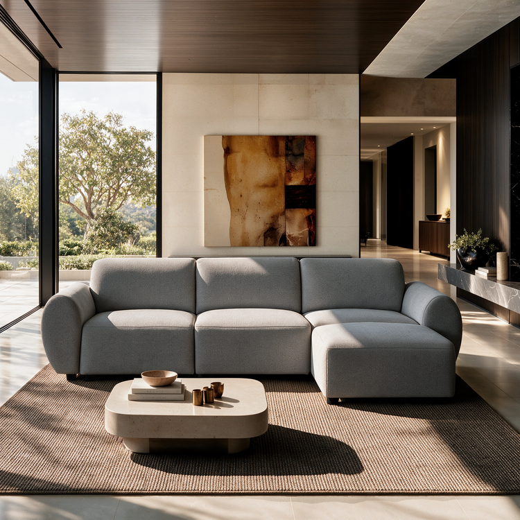 Light gray sectional sofa with rounded arms and a right-side chaise in a sunlit living room with a low coffee table, textured rug, abstract wall art and floor-to-ceiling windows.