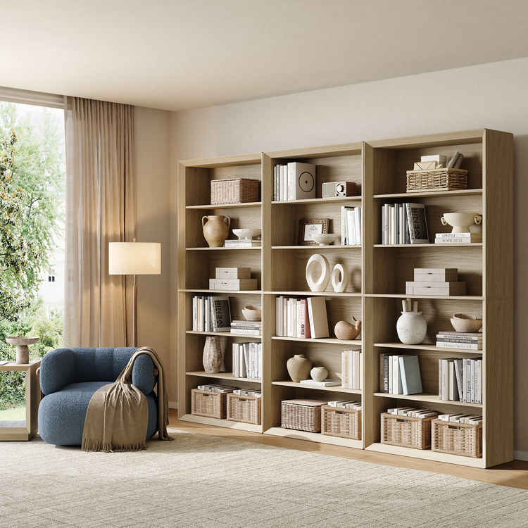 Three tall open bookcases stand side by side with books, baskets, and decor