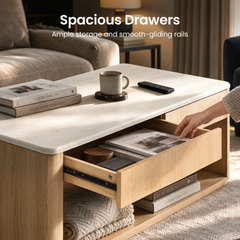 A hand reaches into an open drawer of a light brown coffee table with a cream top, books, a mug and a remote on top, and folded blankets and books on the lower shelf.