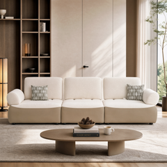 White three-seat sofa with rounded arms and two patterned pillows in a bright living room.
