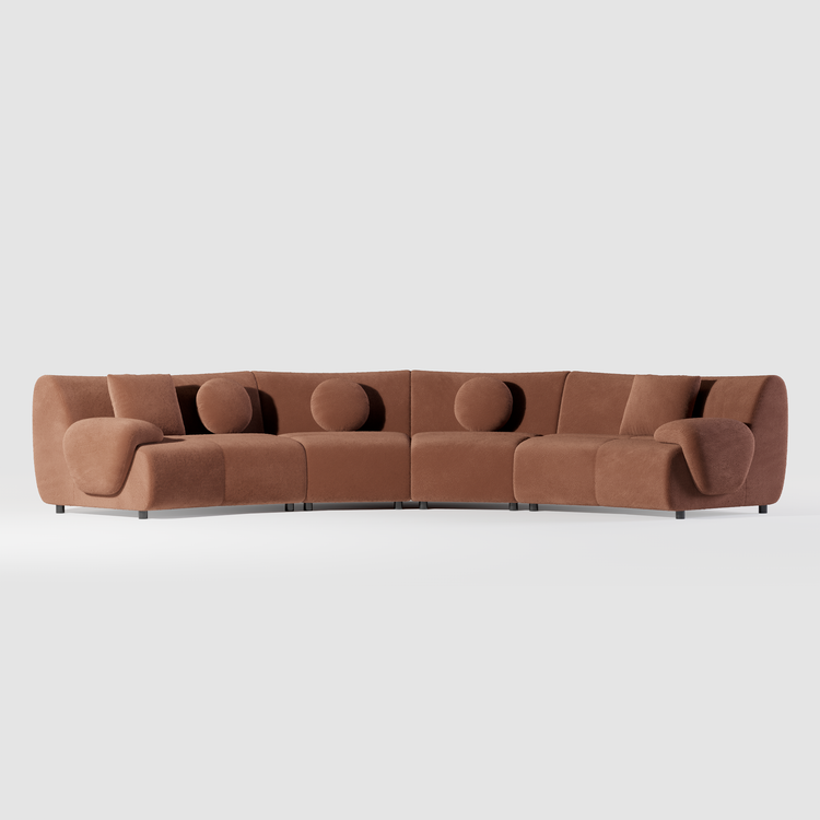 A curved rust-brown sectional sofa with rounded arms, three round cushions, two rectangular cushions and short dark legs.
