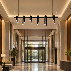 Black pendant light with a horizontal bar and curved, downward-facing illuminated tubes hangs in a tall lobby with glass entrance doors, seating and a reflective floor.