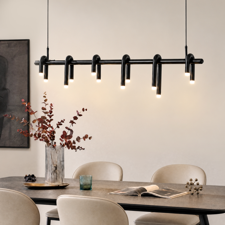 Black pendant light with six curved, looped elements and glowing tips hangs above a dining table with cream chairs, a vase of reddish foliage and an open book.