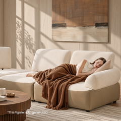 Woman sleeping under a brown blanket on a cream sectional sofa in a sunlit room.