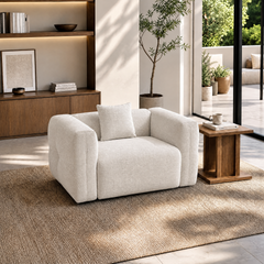 White upholstered armchair with broad arms and a matching cushion in a sunlit room.