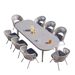 Long gray oval dining table surrounded by woven gray dining chairs on a black background