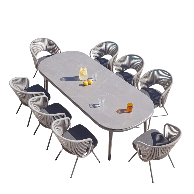 Long gray oval dining table surrounded by woven gray dining chairs on a black background