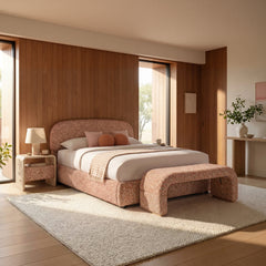 Rust upholstered bed with rounded headboard anchors a sunlit bedroom, A matching curved bench stands at the foot